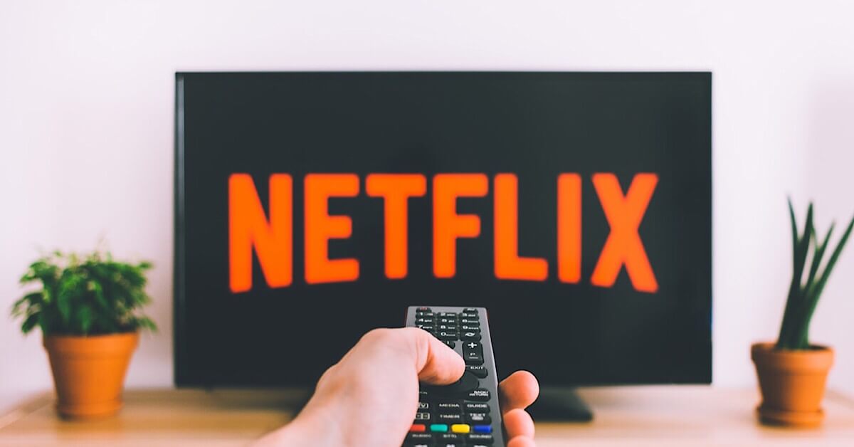 A person pointing a remote at a TV with Netflix on the screen.