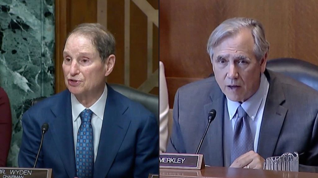 Merkley and Wyden speaking into microphones during official proceedings.