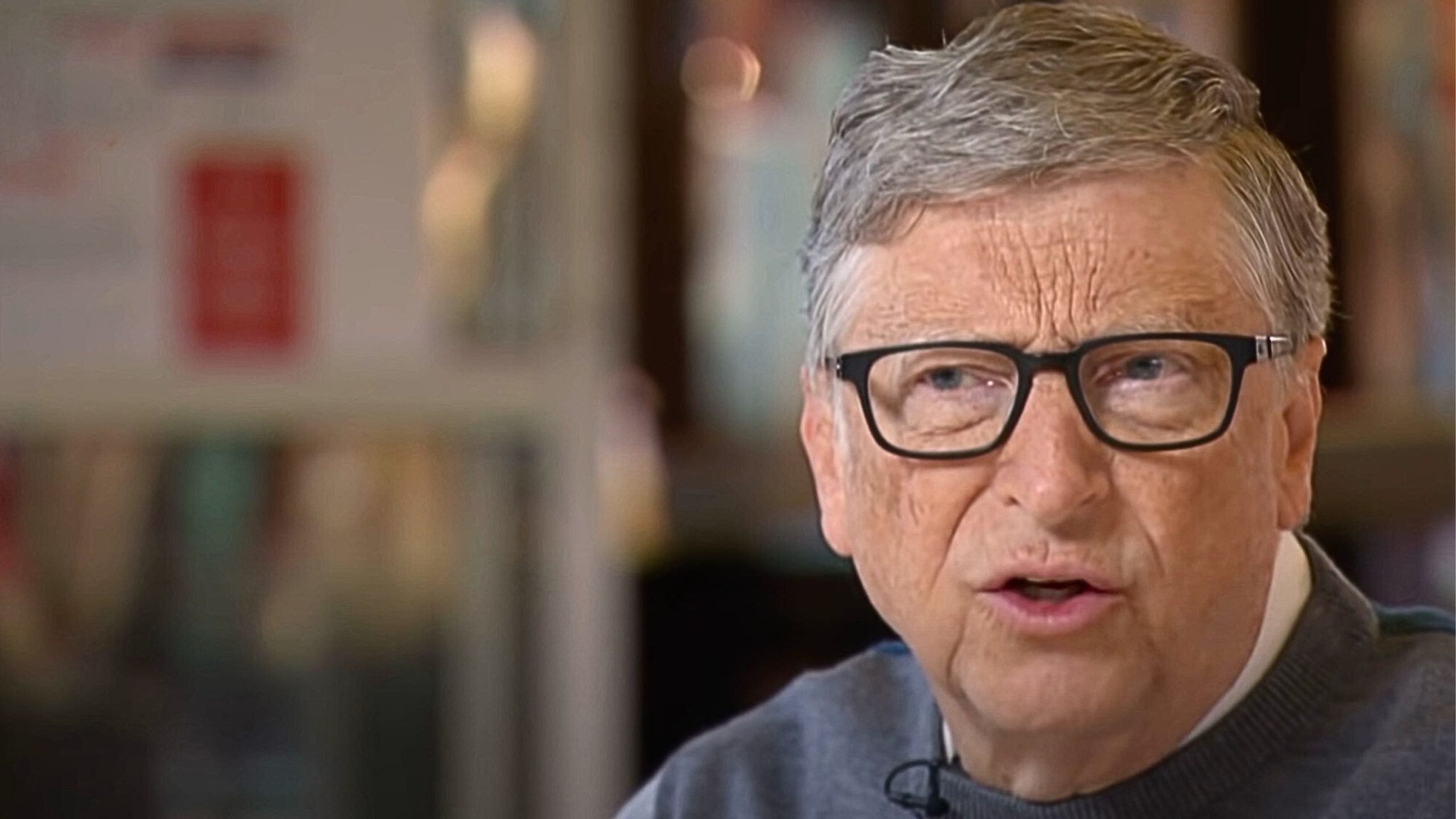 Bill Gates with glasses speaking, with a blurred background.