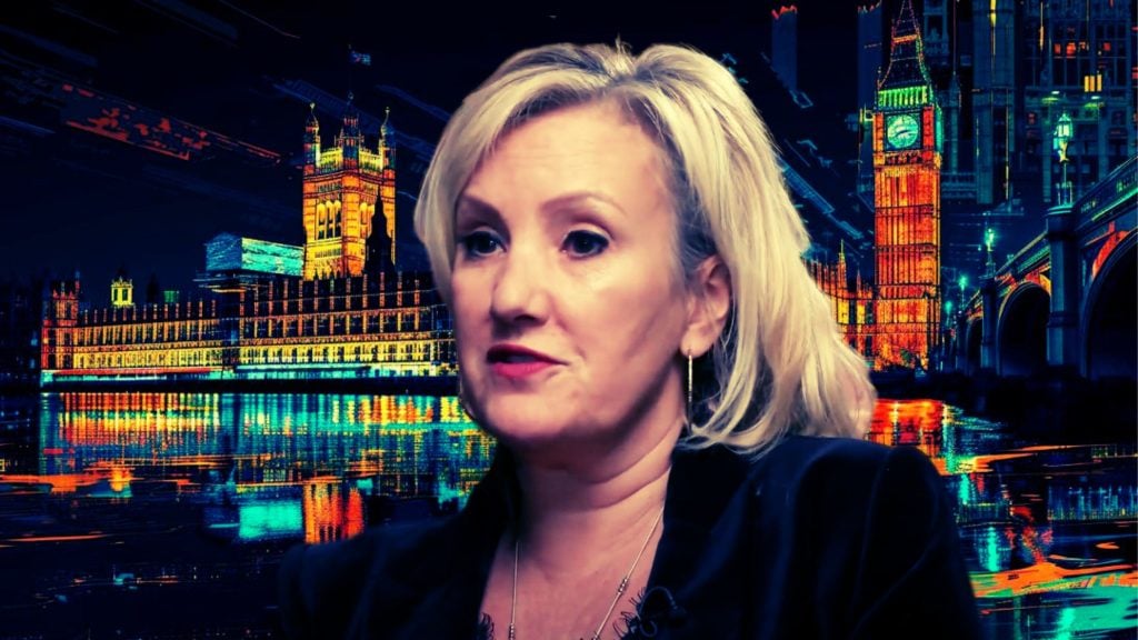 Dinenage speaking with a digitally altered background of Big Ben and the Palace of Westminster at night.