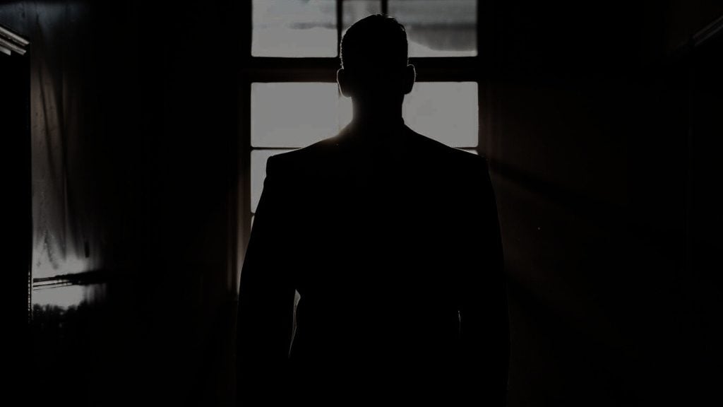 Silhouette of a man in front of a window with daylight streaming through.