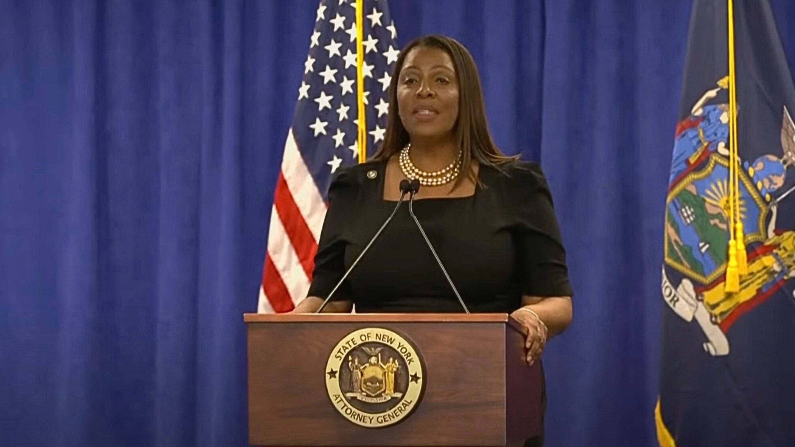 Letitia James at a podium with the seal of the New York Attorney General, flanked by an American flag and the New York state flag, speaking into microphones.