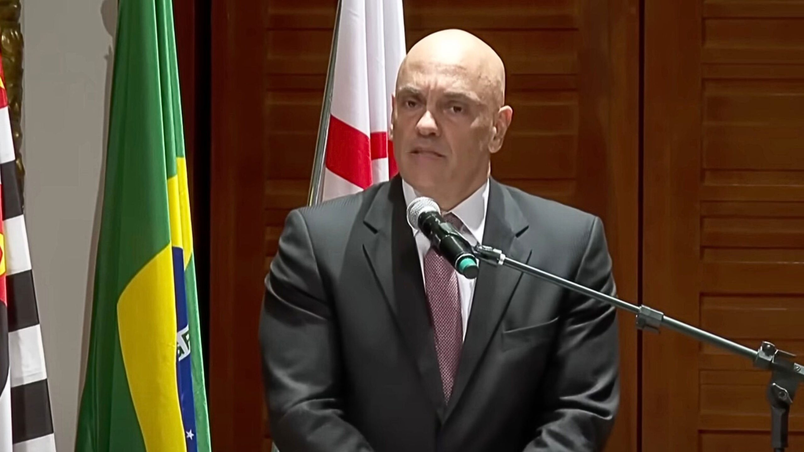 Moraes speaks into a microphone with Brazil and São Paulo state flags in the background.