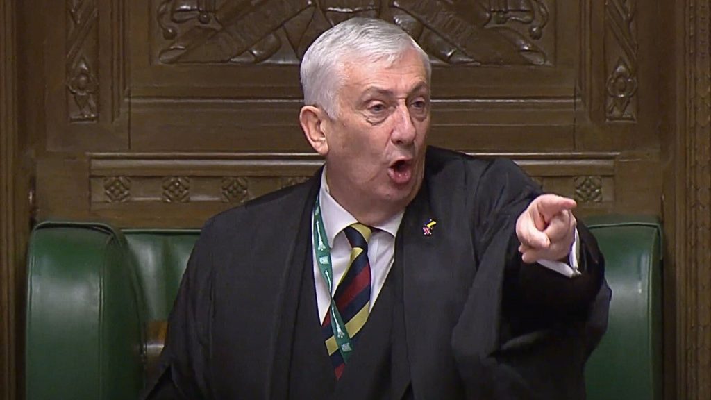 UK House Speaker Lindsey Hoyle in a suit and tie shouting and pointing, sitting in a formal setting with wooden decorative panels in the background.