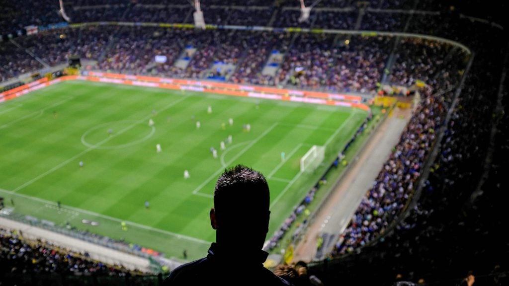 Silhouette of a person watching a soccer match in a packed stadium at night.