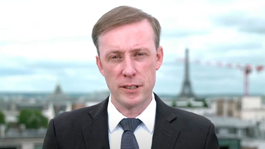 Jake Sullivan wearing a suit and tie, standing outdoors with the Eiffel Tower in the background.