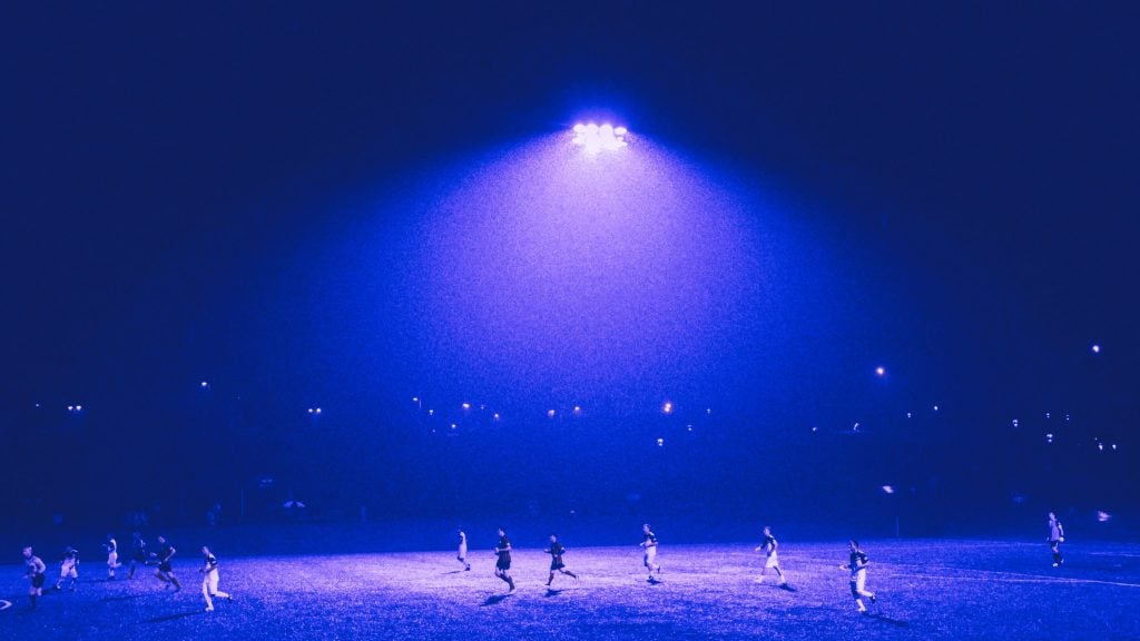 Soccer players on a field under bright stadium lights at night.