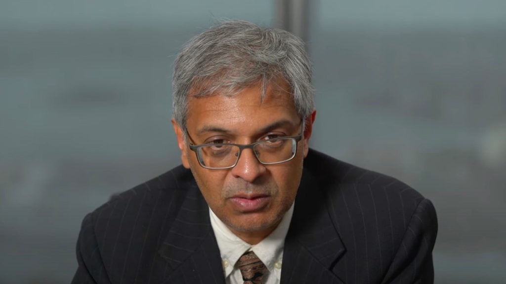 Bhattacharya and glasses wearing a suit and tie.