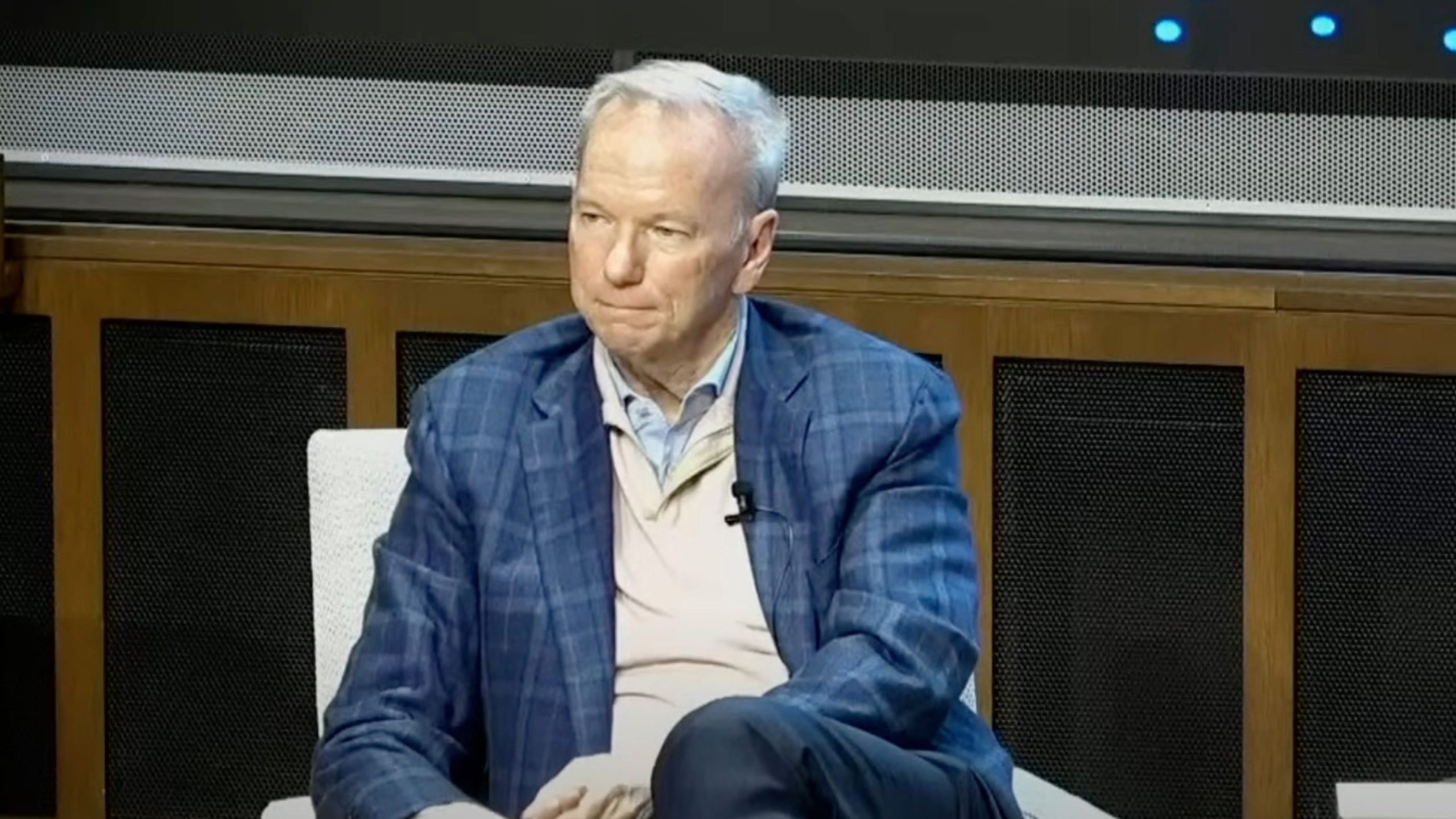 Eric Schmidt in a checkered blue suit sitting in a chair, with a microphone clipped to his sweater.