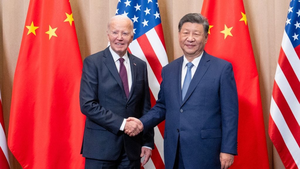 Biden and Xi shaking hands in front of American and Chinese flags.