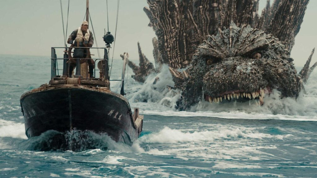 A fishing boat on the ocean is pursued by a giant Godzilla with spiky scales and sharp teeth emerging from the water.