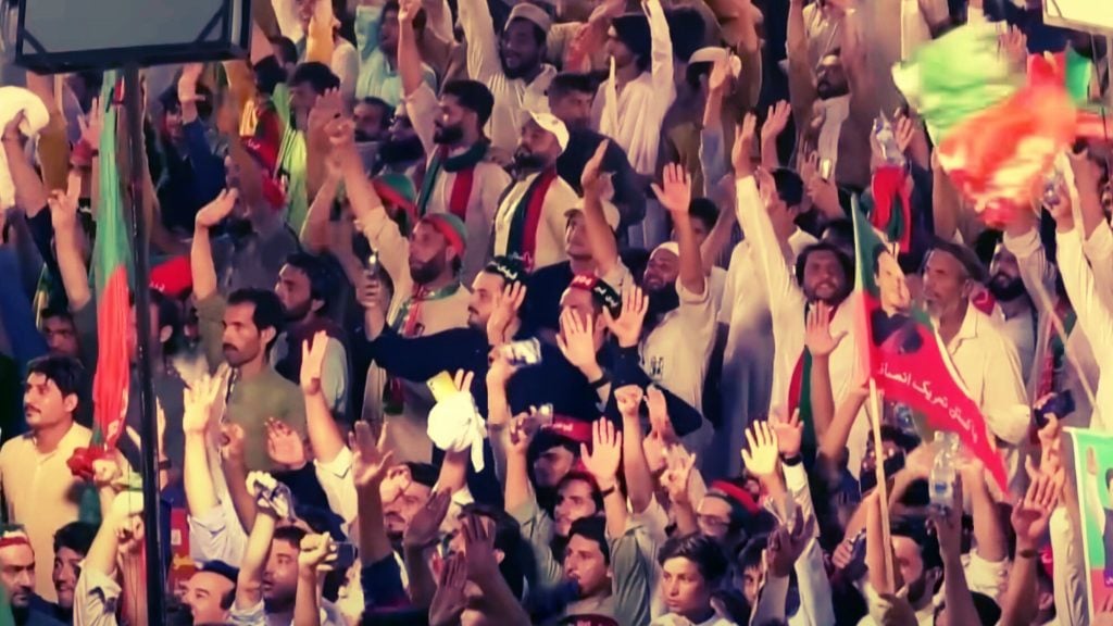 A large crowd of people raising their hands and waving flags at a rally.