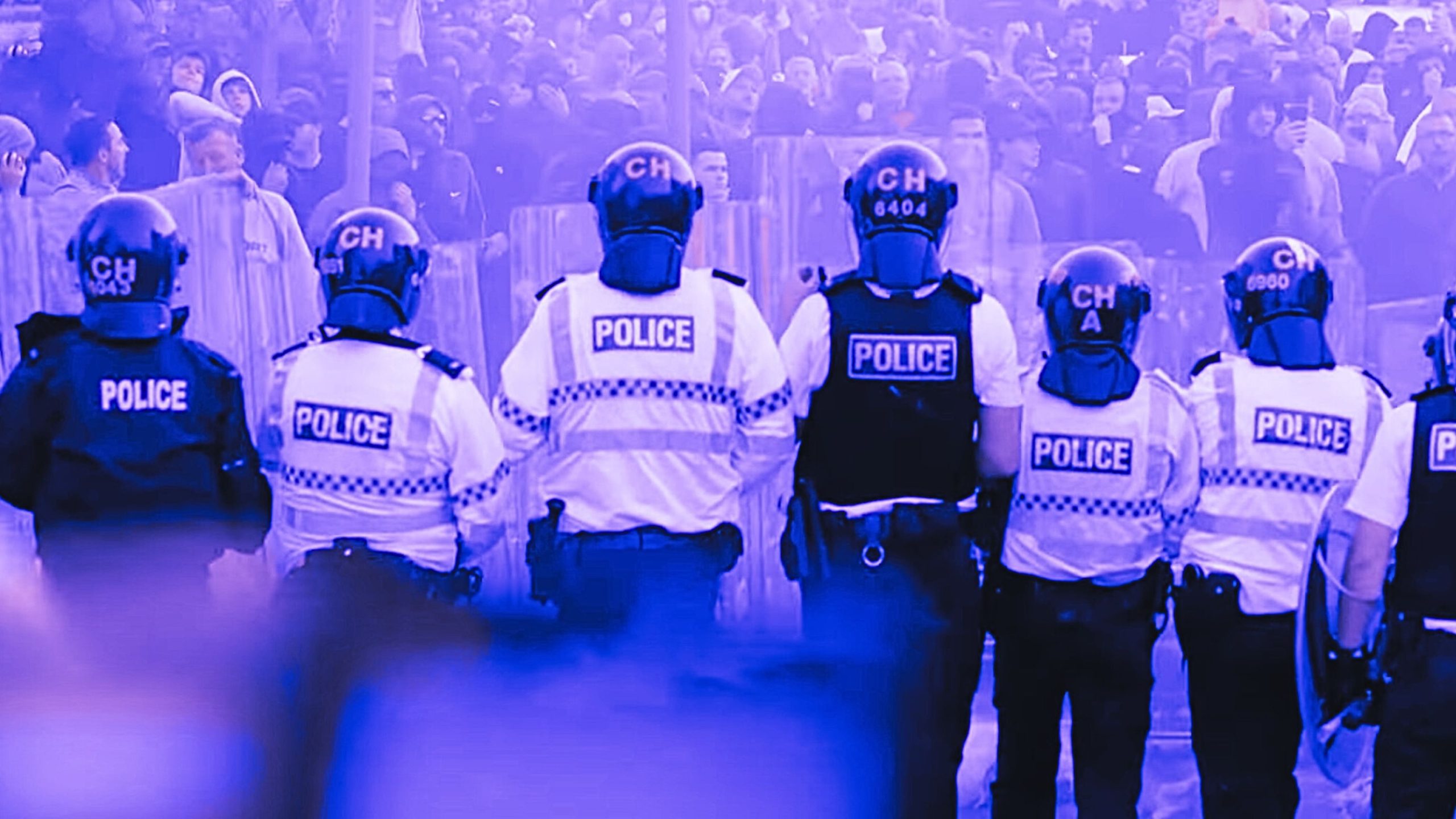 Police officers in riot gear standing in a line facing a crowd.