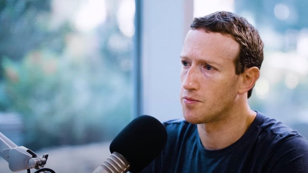 Zuckerberg into a microphone during an interview or podcast, with a blurred background.