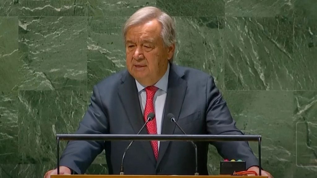 Antonio Guterres in a suit speaks at a podium with a green marble background.