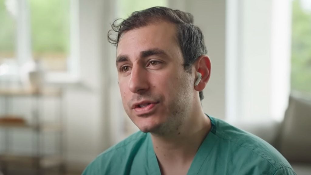 Dr. Haim with short brown hair wearing green scrubs and a wireless earbud.