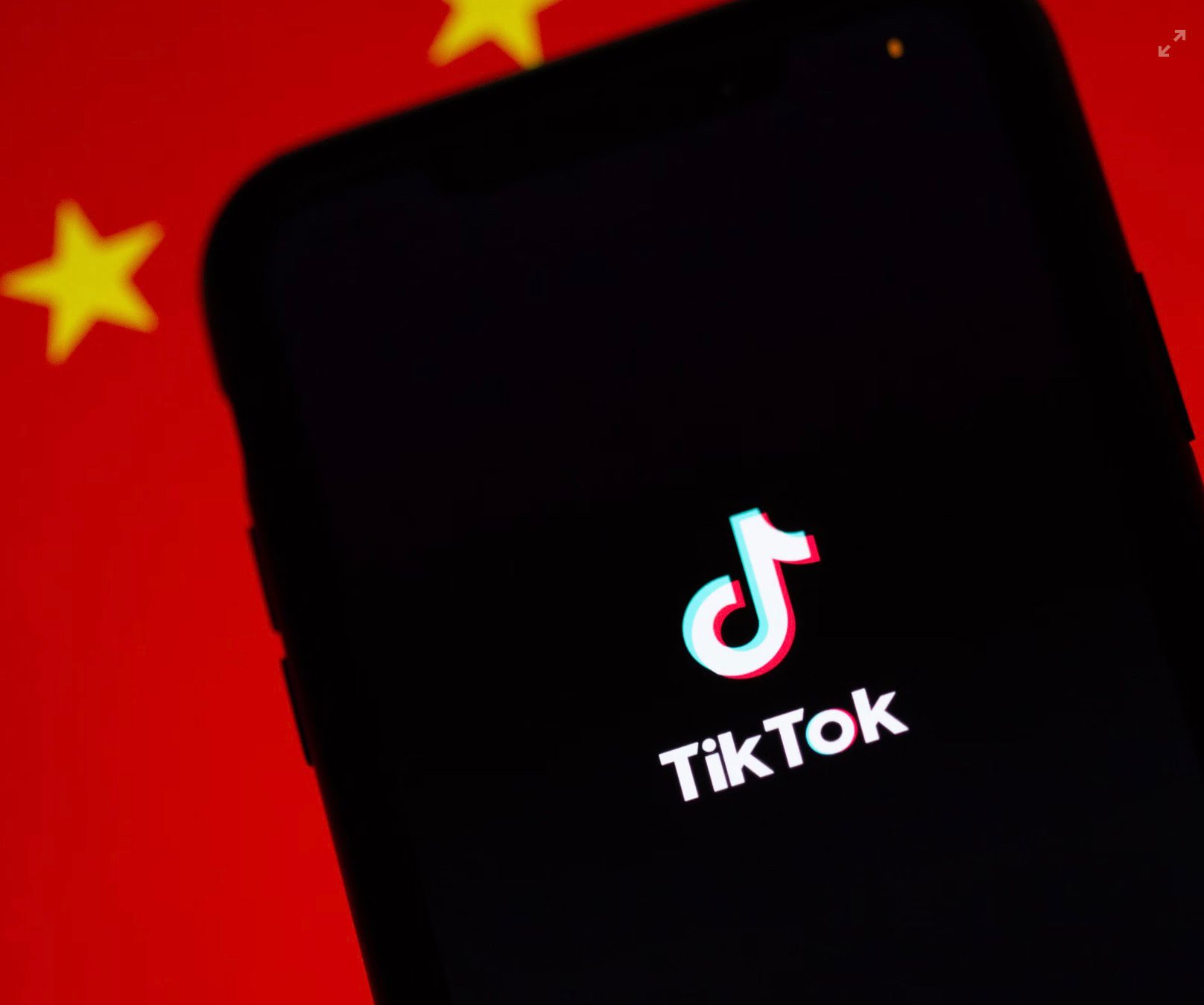 A smartphone screen displaying the TikTok logo with a blurred Chinese flag in the background.