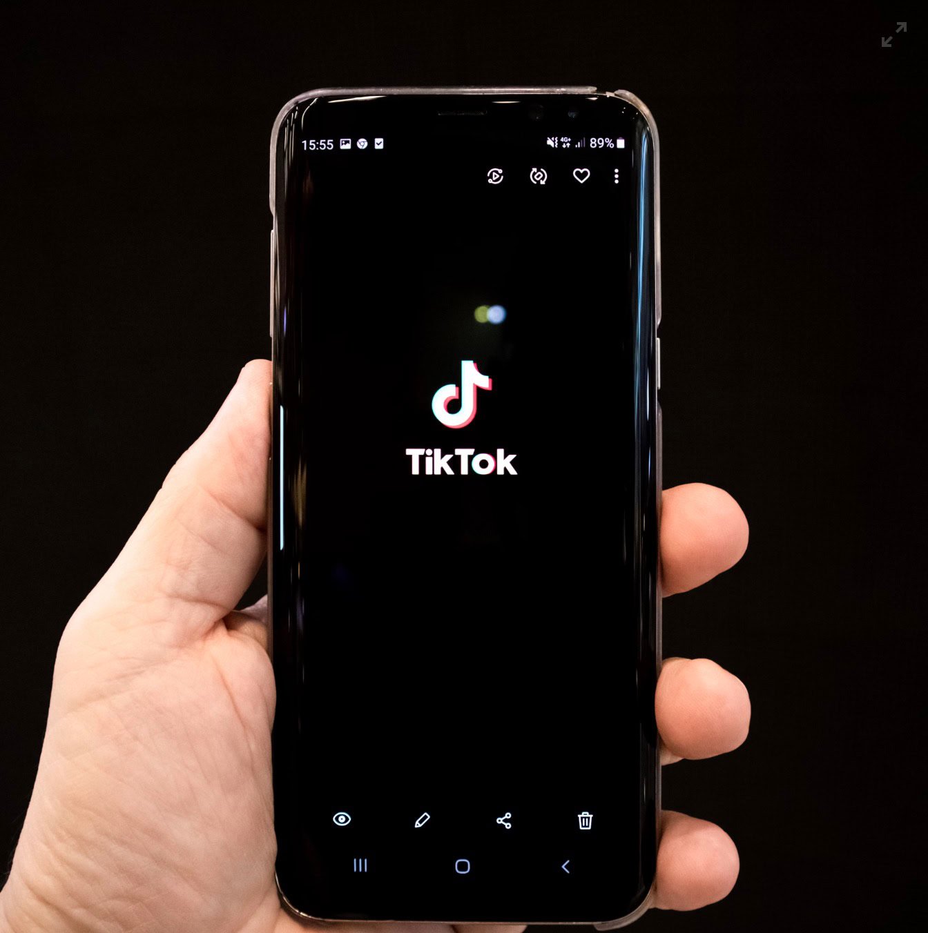 A hand holding a smartphone displaying the TikTok app logo on the screen.