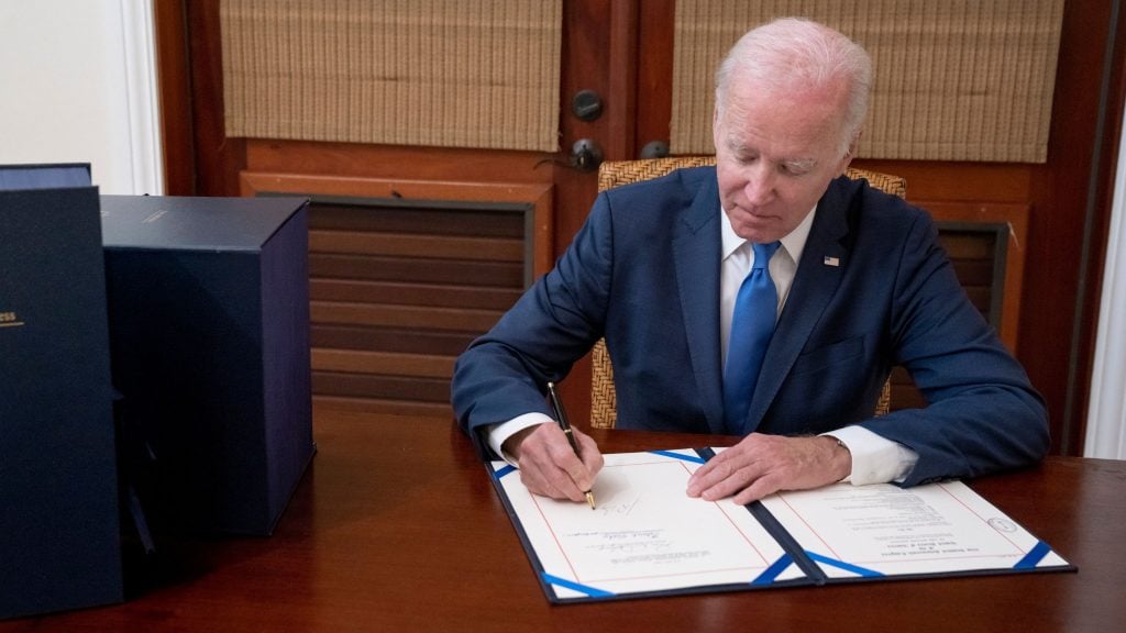 Biden in a suit signing a document at a desk.