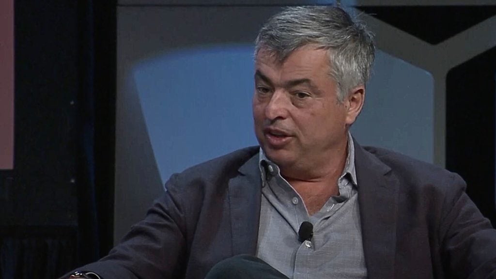 Eddie Cue speaking, wearing a suit jacket and a microphone attached to his shirt.