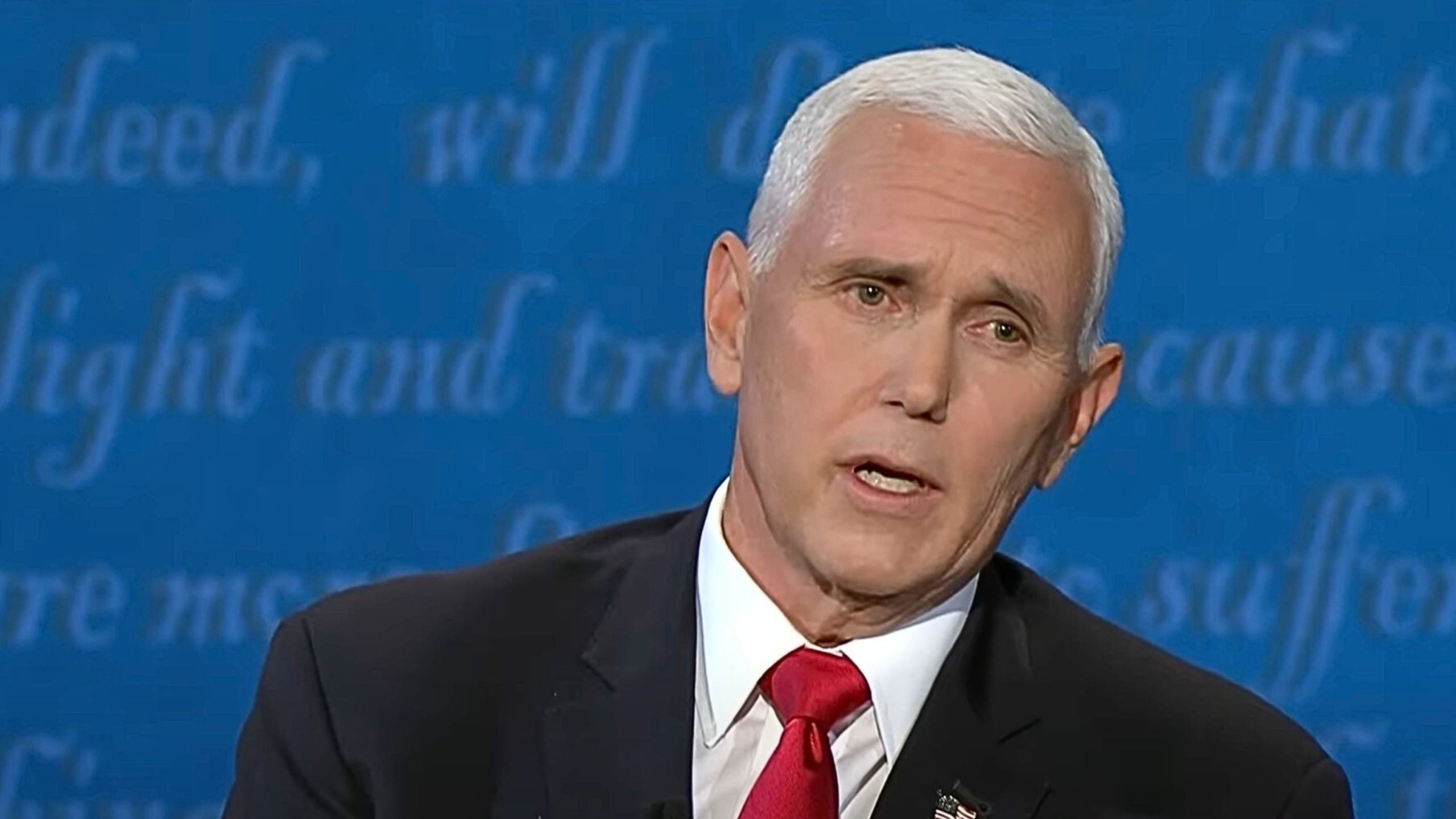 Pence in a suit and red tie speaking, with a blue background containing text.