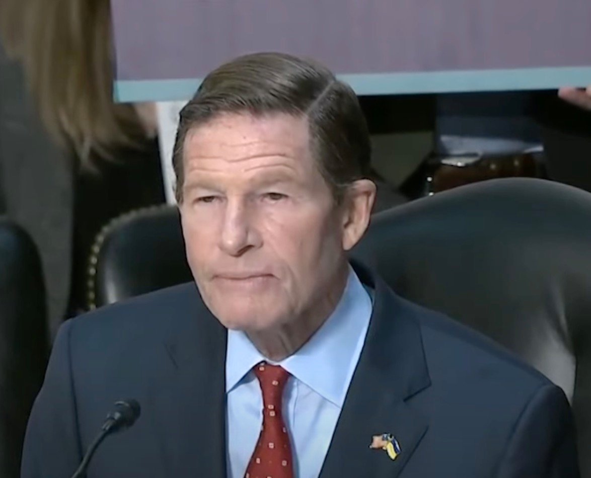 Senator Blumenthal in a suit and red tie sitting in a chair, speaking into a microphone.