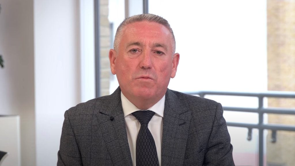 Jamieson in a suit and tie sits in an office with a window in the background.