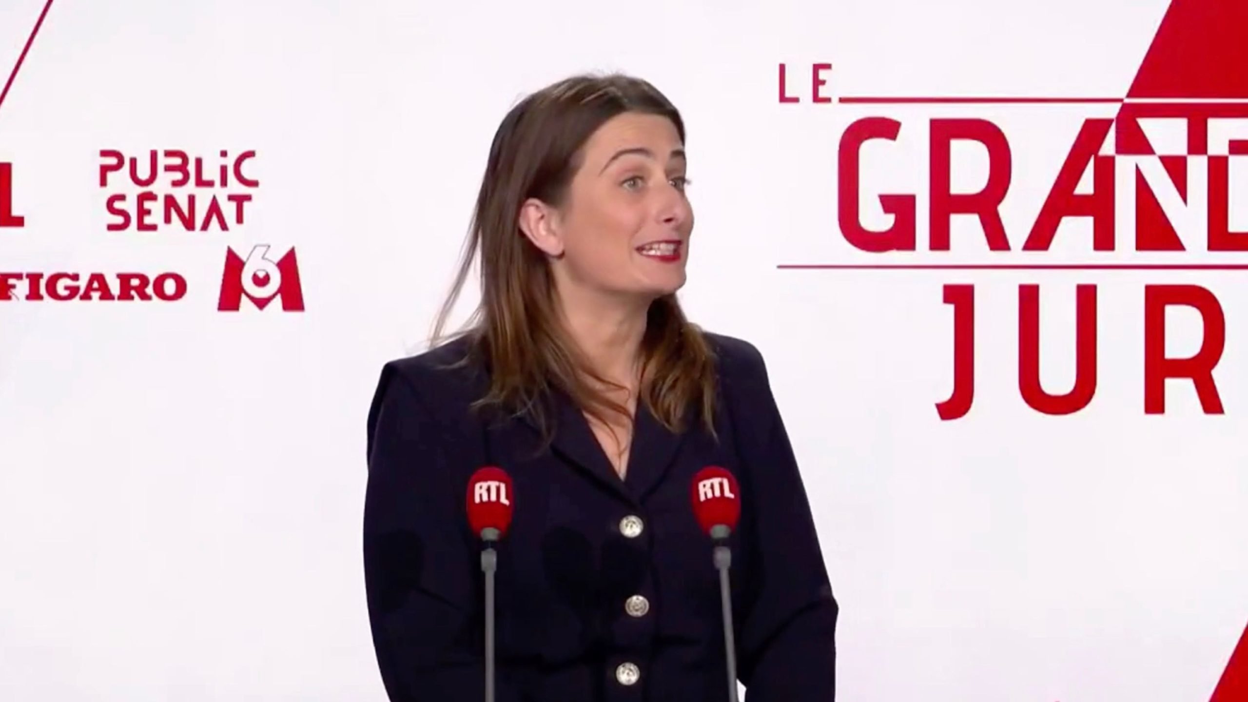 Tondelier speaking at a podium with RTL microphones, in front of a backdrop featuring "Le Grand Jury" and various media logos.