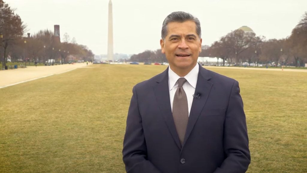 Xavier Becerra in a suit standing on a lawn with the Washington Monument in the background.