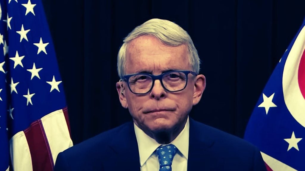 DeWine with glasses and white hair in front of American and Ohio flags.