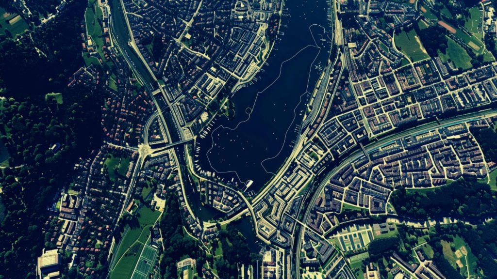 Aerial view of a city layout featuring a large body of water surrounded by urban infrastructure and green areas.