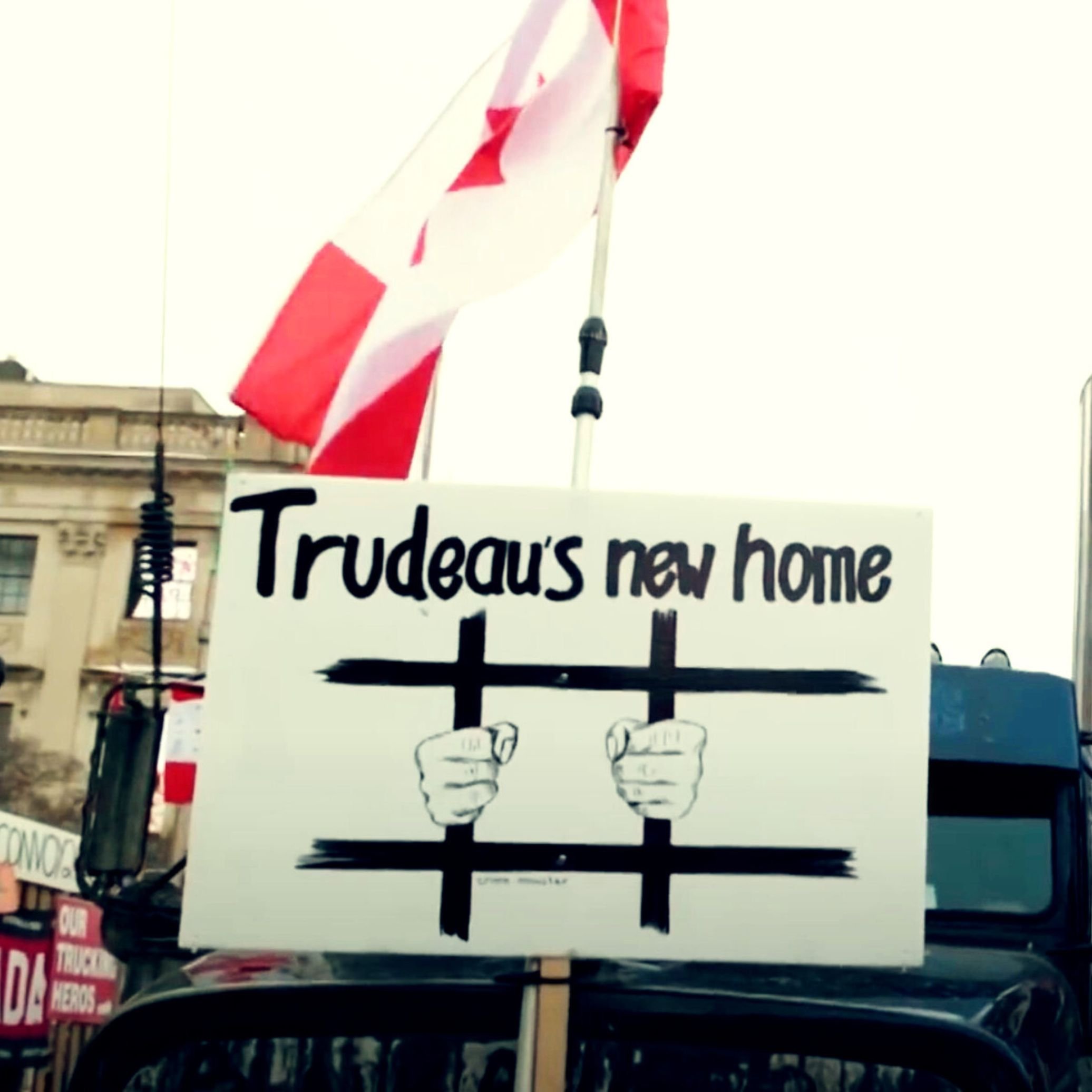 Sign saying "Trudeau's new home" with an illustration of hands gripping prison bars, beneath a Canadian flag.