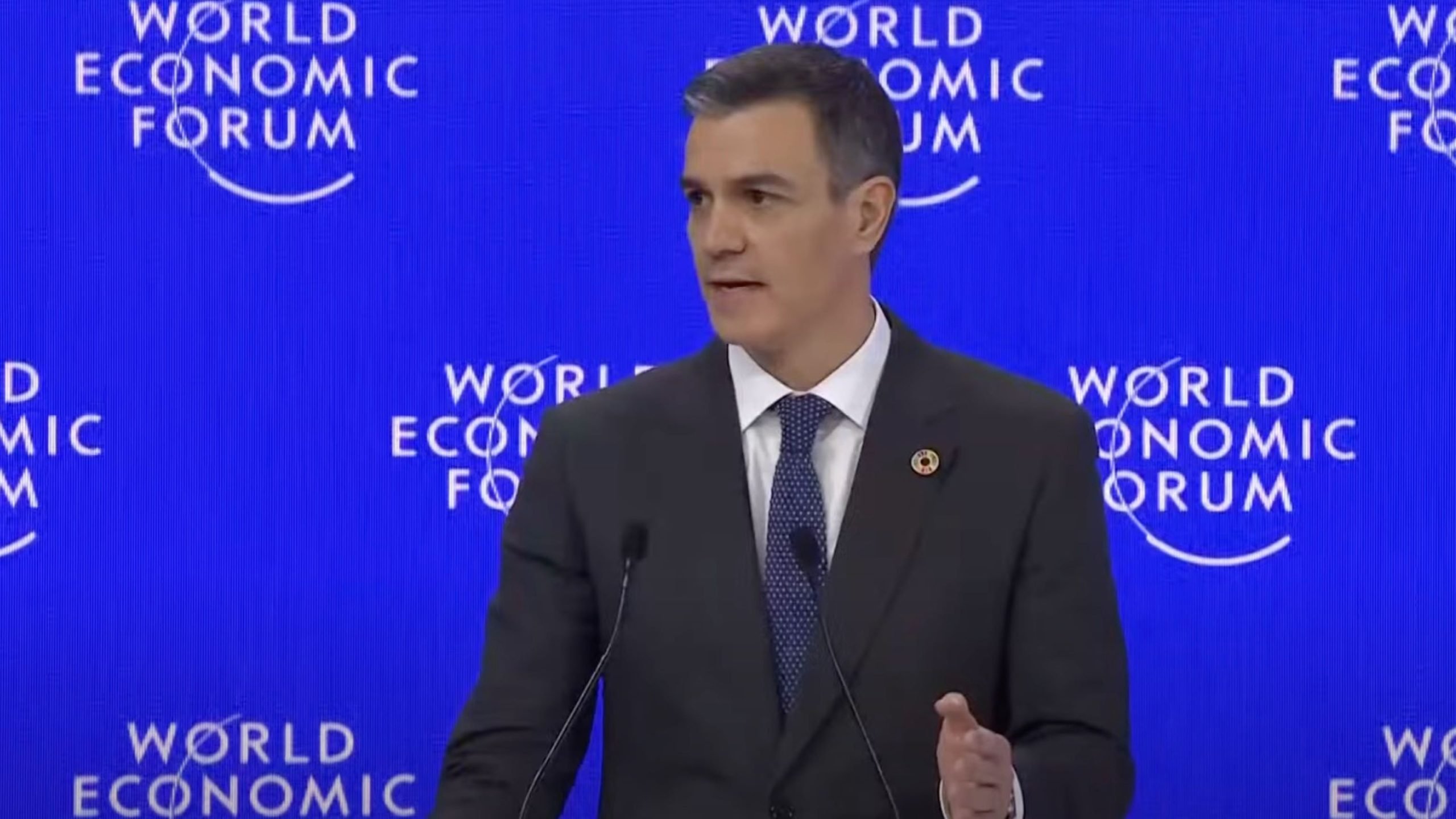 Sanchez in a suit speaks at a podium with "World Economic Forum" displayed in the background.