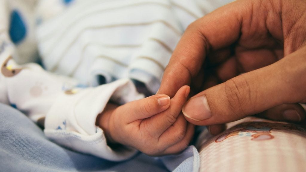 Close-up of an adult hand gently holding a newborn baby's hand.