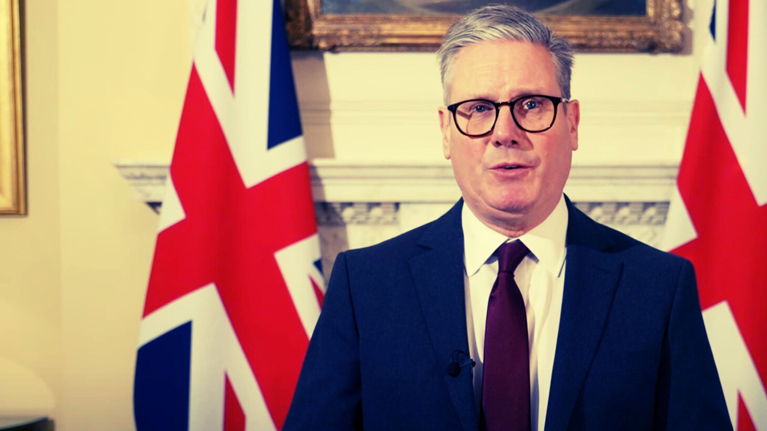 Starmer in a suit and tie stands in front of a British flag.