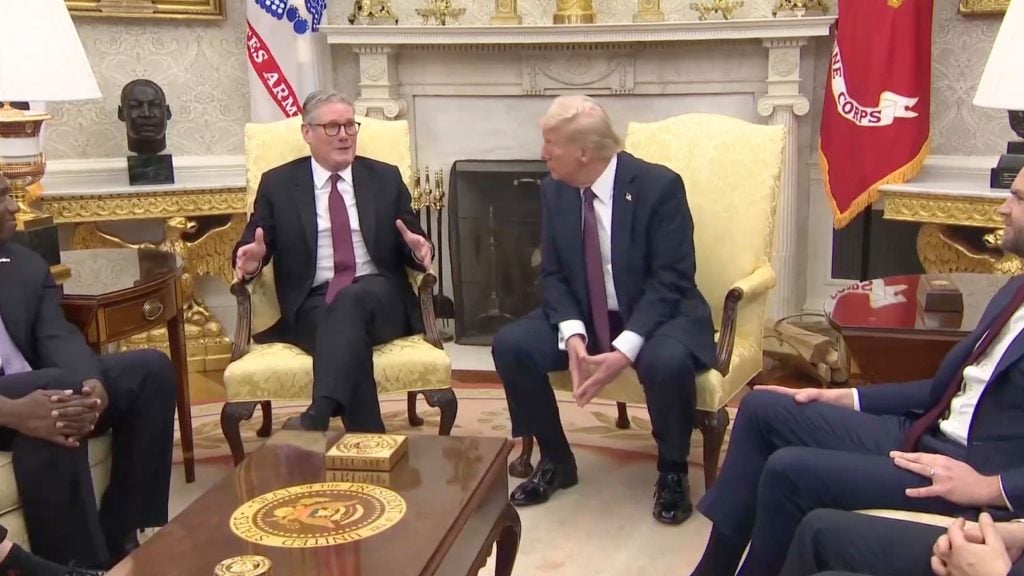 Starmer, Trump and more in formal suits are sitting in a well-decorated office room, featuring a fireplace, ornate furnishings, and a bust sculpture on a mantel. Seals and flags suggest a governmental setting.