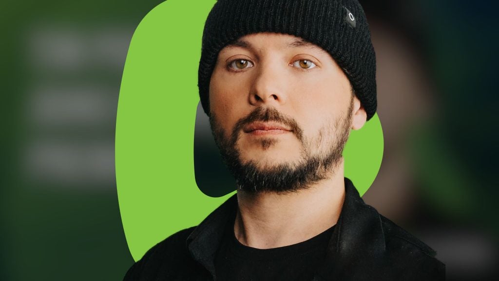 Tim Pool wearing a black beanie and jacket with a green background.