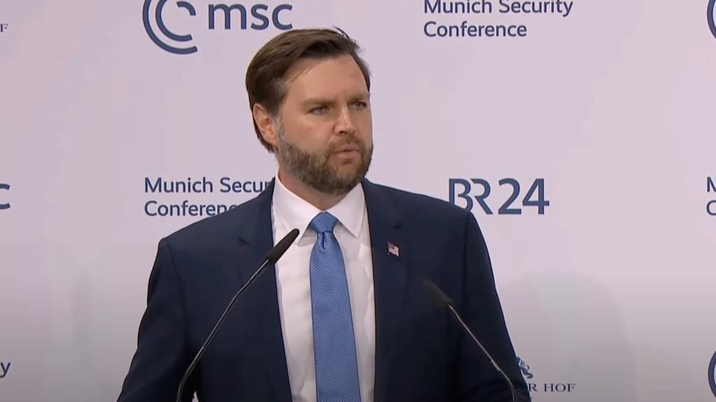 JF Vance in a suit and tie speaks at a podium, with the backdrop displaying the logo and text of the Munich Security Conference.