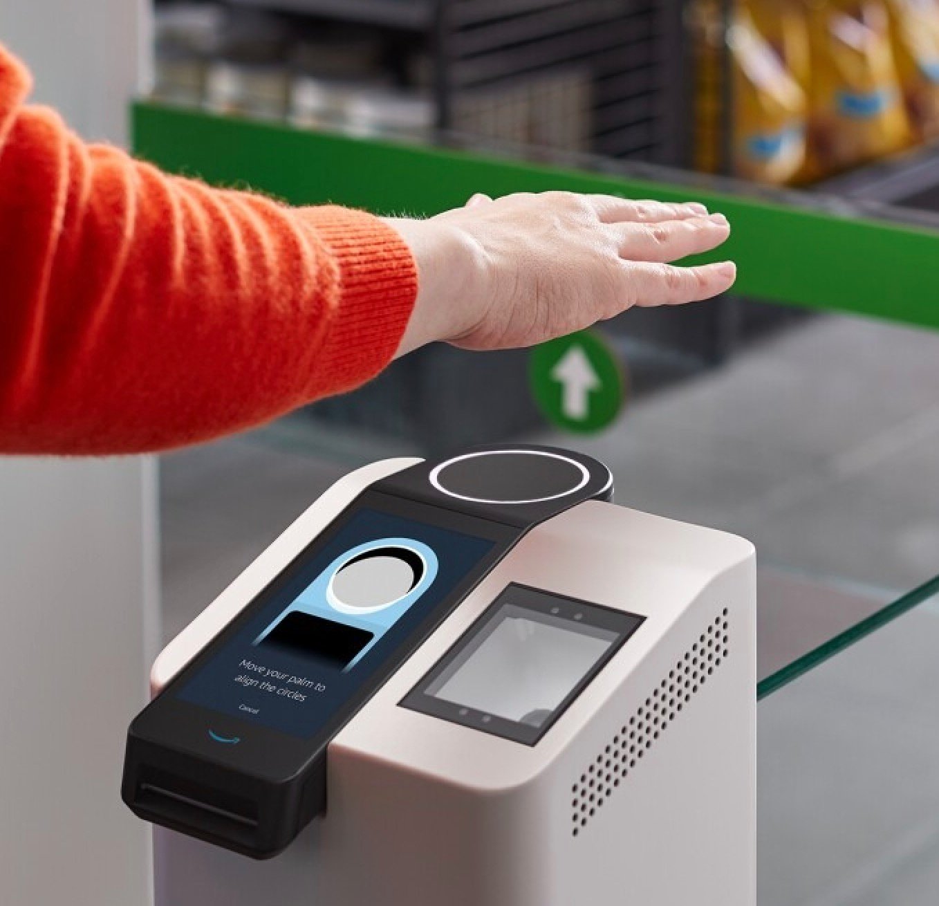 A person uses a biometric device for palm scanning, with a screen indicating it's ready for palm alignment, in a retail environment.