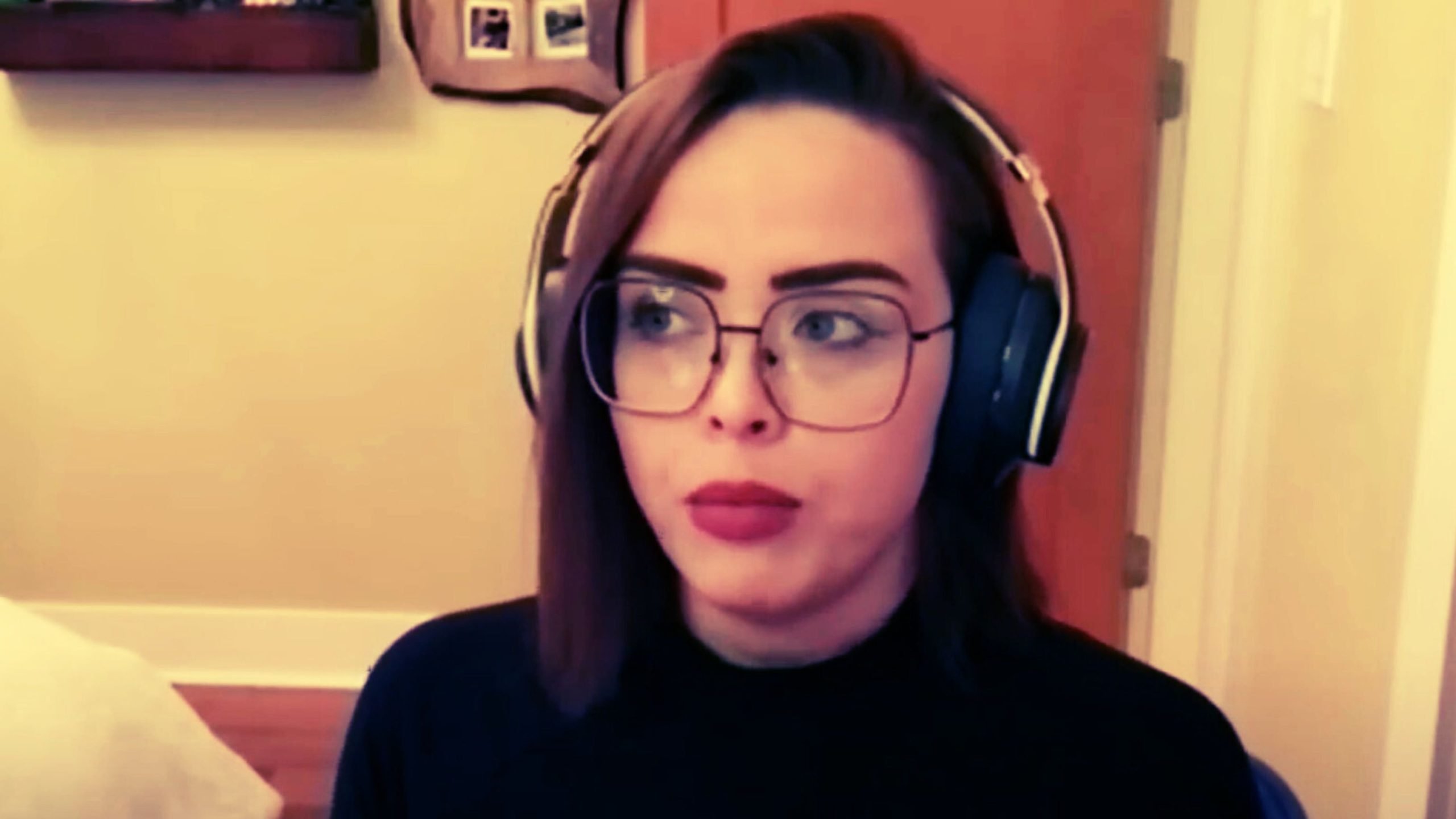 Hamm wearing large glasses and headphones, looking slightly to the side, in an interior setting with a doorway and wall in the background.