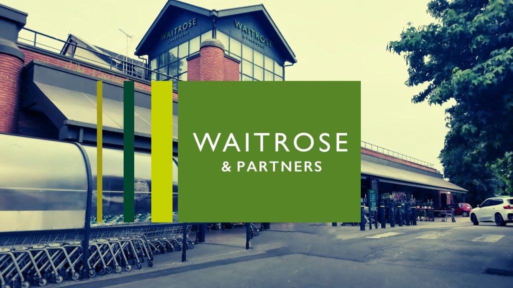 Exterior view of a Waitrose & Partners supermarket with parked shopping carts and a green logo displayed prominently in the foreground.