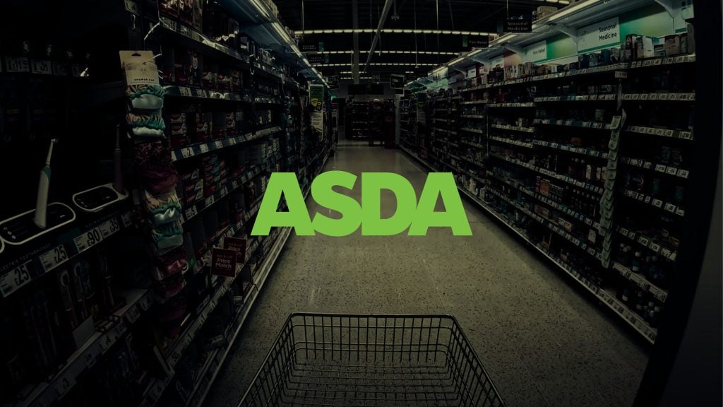 View down an empty supermarket aisle with shelves stocked on both sides and a shopping cart in the foreground, overlaid with the green ASDA logo in the center