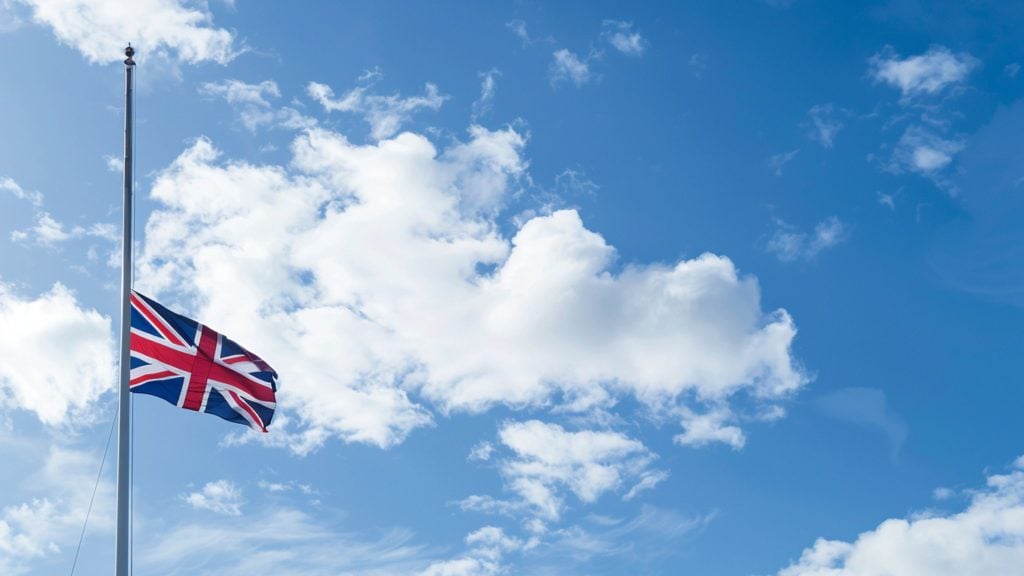 Union Jack flag flying at half-mast against a blue sky with scattered white clouds
