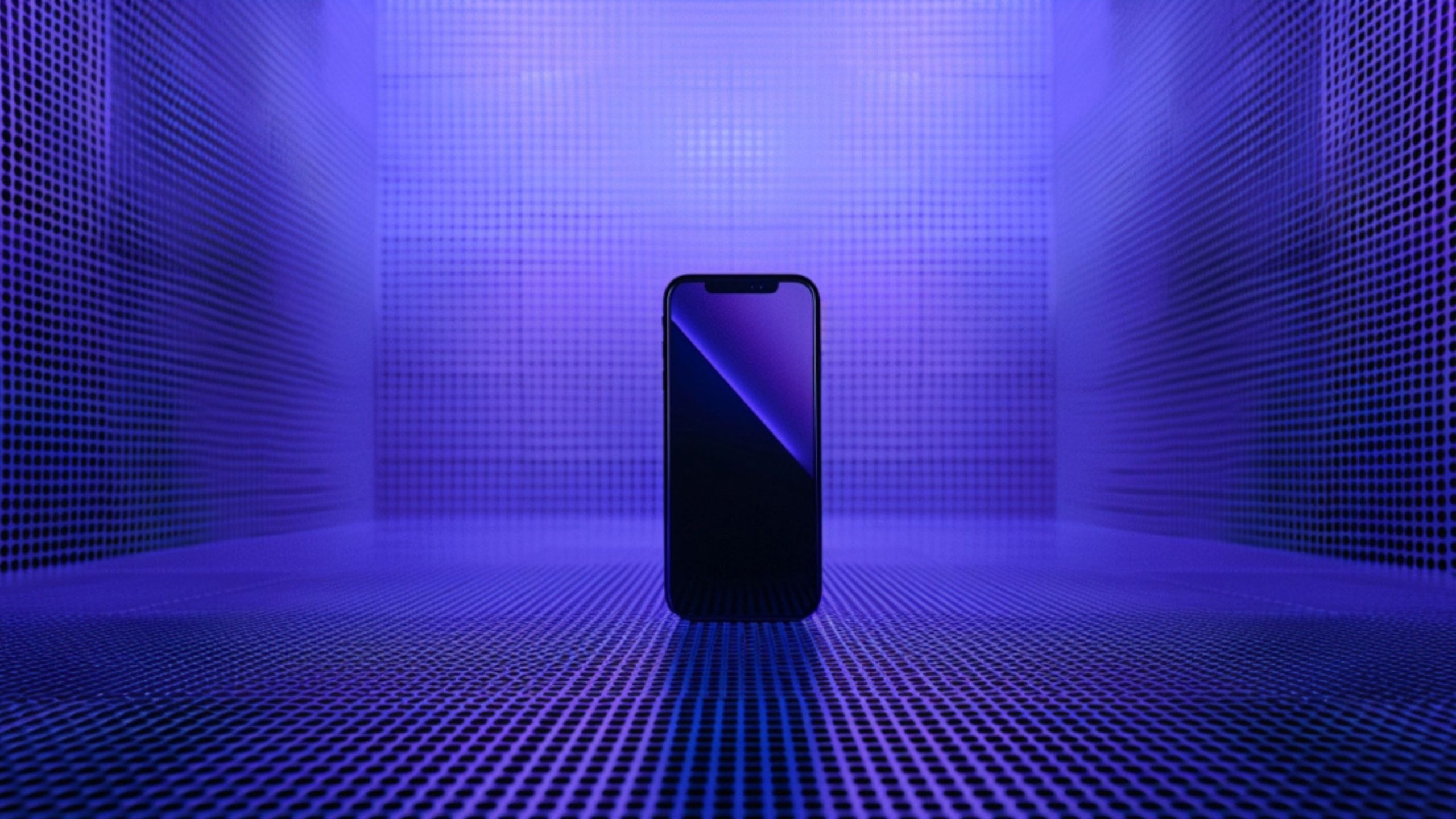 A modern smartphone standing upright in the center of a room with walls, floor, and ceiling covered in a grid of small circular perforations, illuminated by blue and purple lighting.