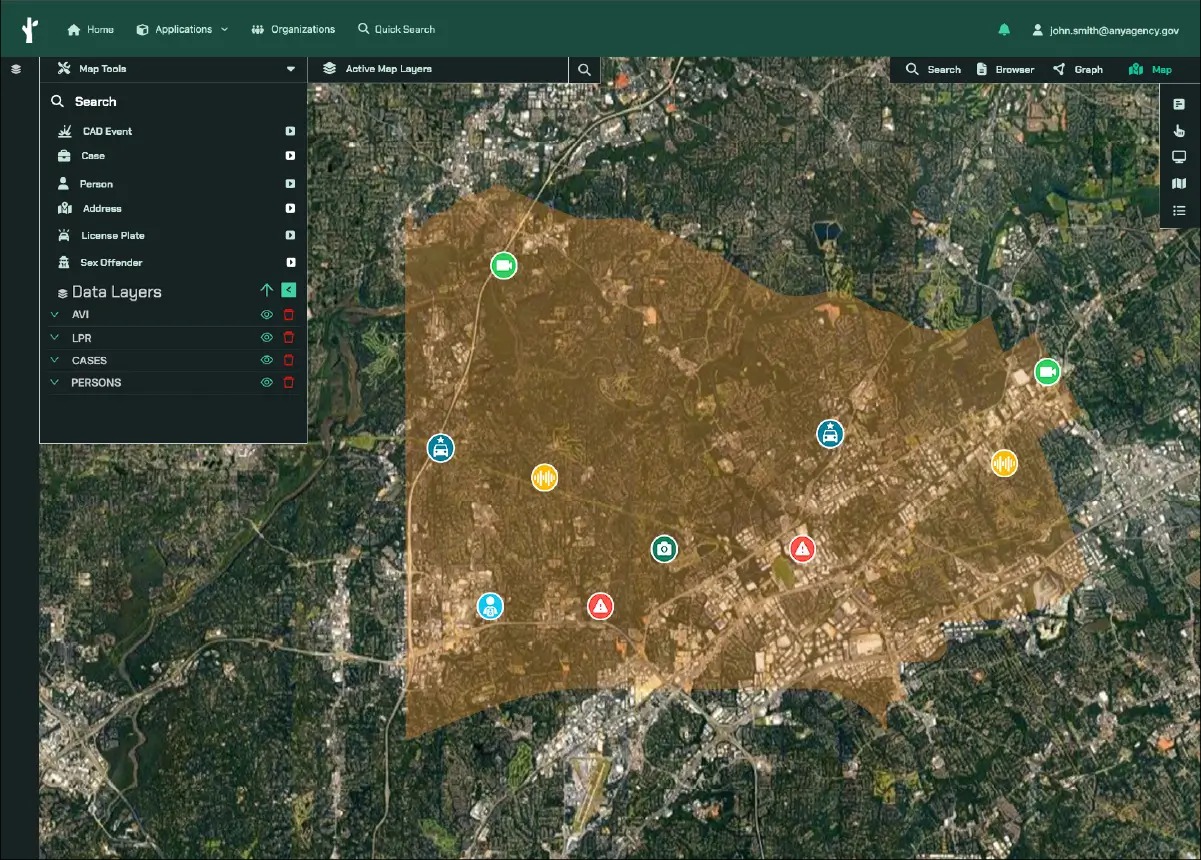 Interactive map interface showing a satellite view of a city with a highlighted brown area representing a data layer; map icons include cameras, alerts, audio signals, and person markers; left panel lists map tools like Search, CAD Event, Case, Person, Address, License Plate, Sex Offender, and data layers such as AVI, LPR, CASES, PERSONS; top bar includes navigation and search options with a user email displayed.