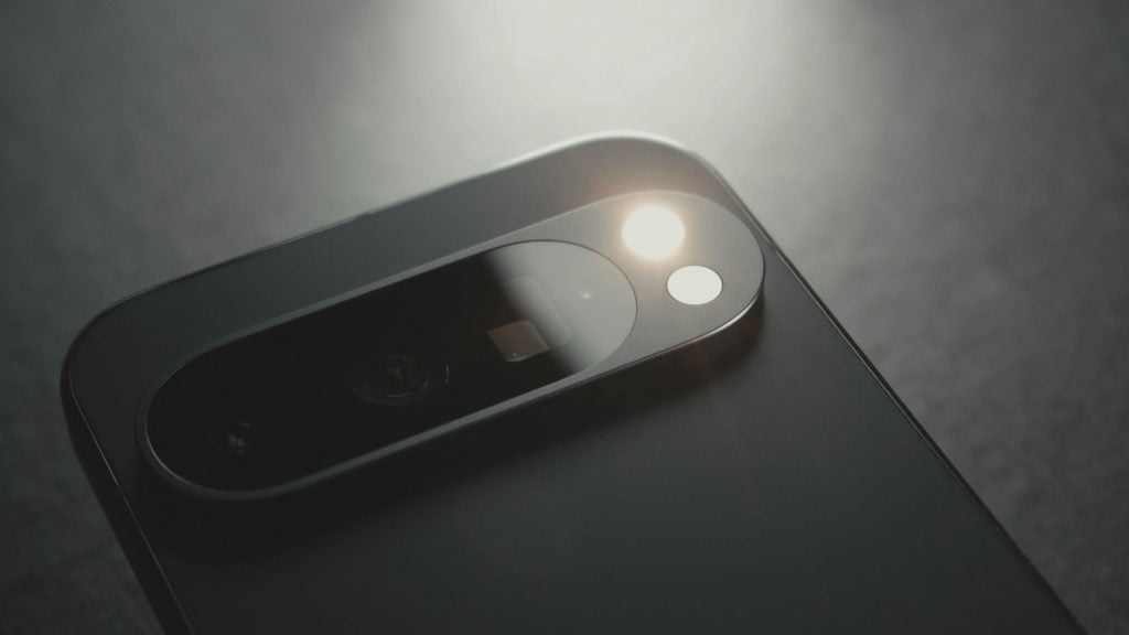 Close-up of a smartphone's dual rear camera module with one flash illuminated on a dark surface