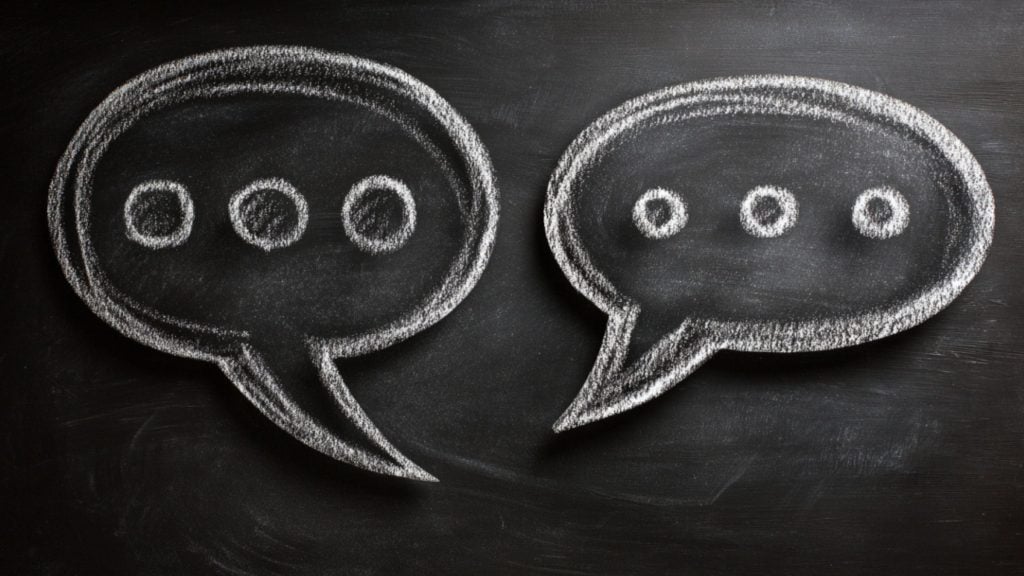 Two white chalk speech bubbles with three dots inside each, drawn on a black chalkboard, symbolizing conversation or communication.