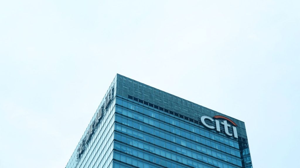Top corner of a modern glass skyscraper with the Citi logo on the upper right side against a clear sky