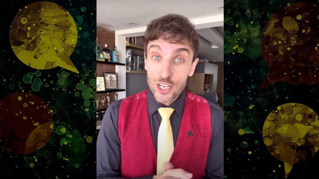 Leo Lins comedian with short brown hair, wearing a red vest over a black shirt and a yellow tie, speaking indoors with shelves and various items in the background.