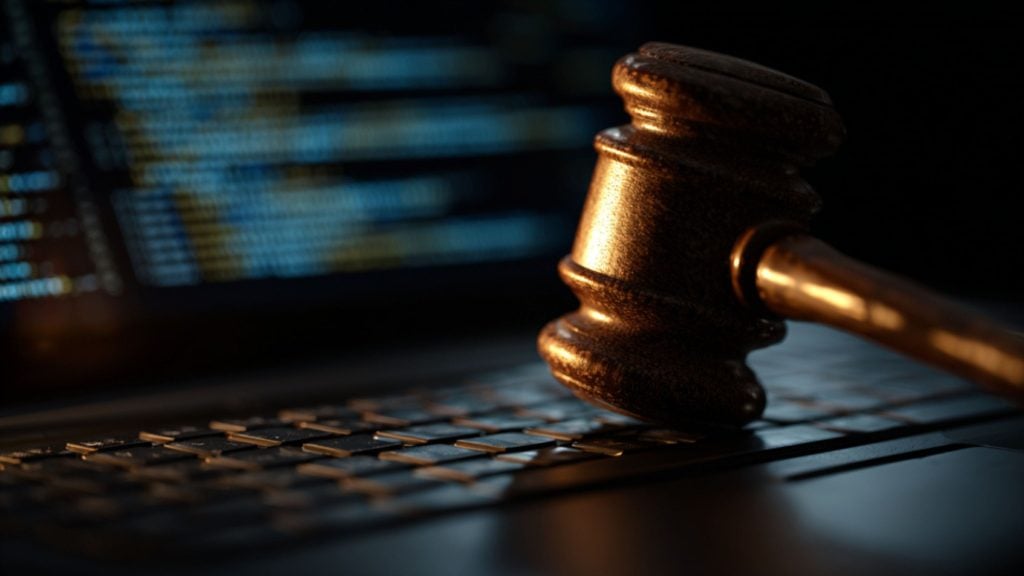 Close-up of a judge's gavel resting on a laptop keyboard with a blurred screen showing lines of code in the background, symbolizing digital law or cyber justice.